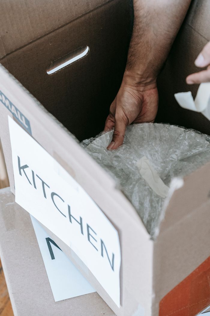 Gros plan sur l’emballage d’objets de cuisine pour un déménagement dans une boîte en carton étiquetée, à l’intérieur.